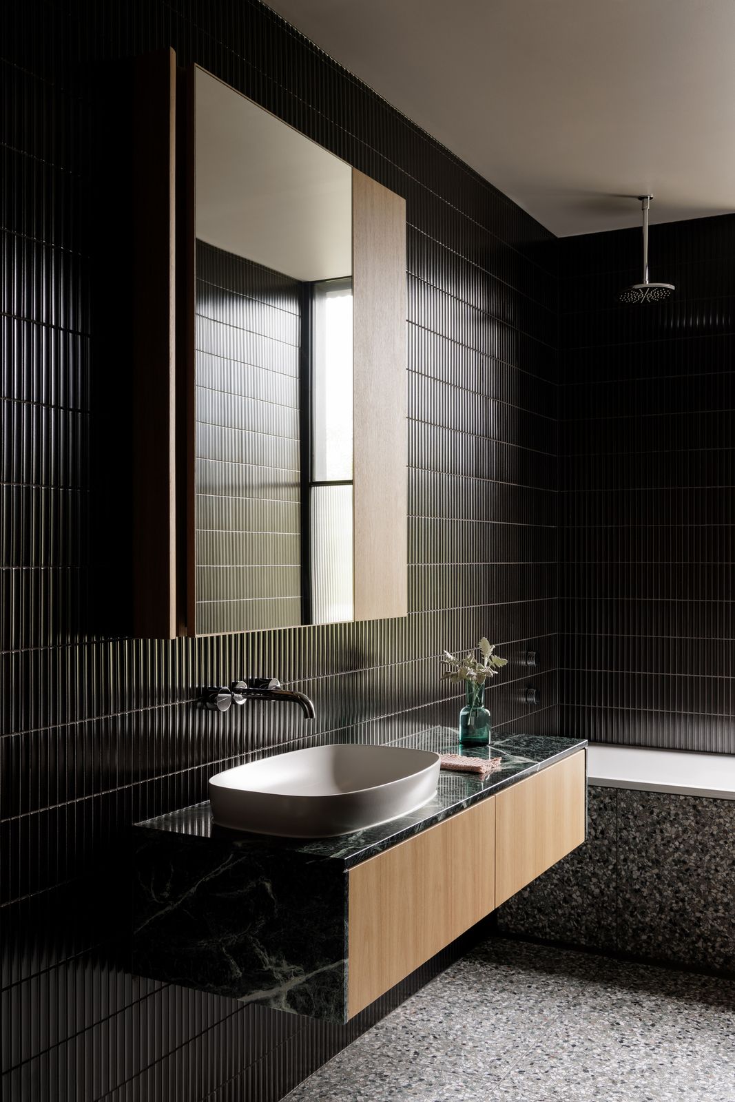 Borrowed Garden House bathroom with wall tapware, basin, bath, stone vanity, and black wall tiles